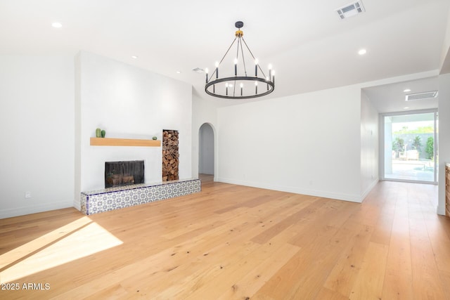 16227 N 63rd Pl, Scottsdale, AZ 85254 - unfurnished living room featuring arched walkways, a chandelier, light wood-style flooring, a tiled fireplace, and baseboards