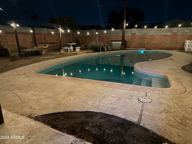 pool at night featuring a patio area