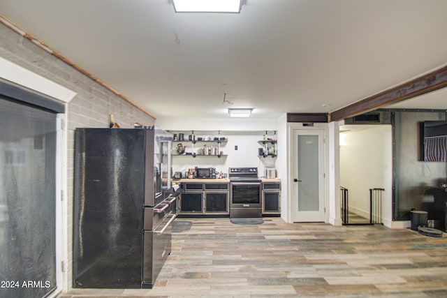 kitchen featuring black fridge, stainless steel electric range oven, light wood-type flooring, and brick wall