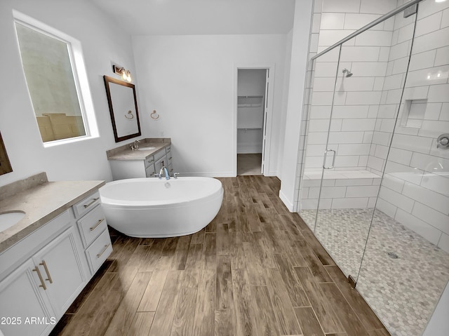bathroom featuring a stall shower, two vanities, wood finished floors, a spacious closet, and a sink