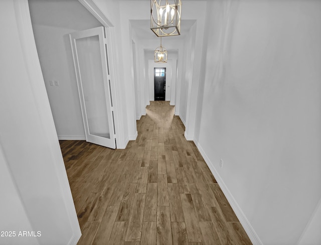 hallway with a notable chandelier, wood finished floors, and baseboards