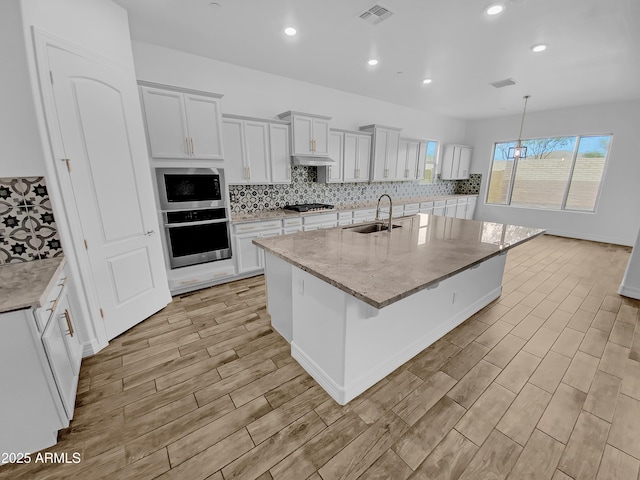 kitchen featuring gas cooktop, oven, a sink, visible vents, and white cabinetry