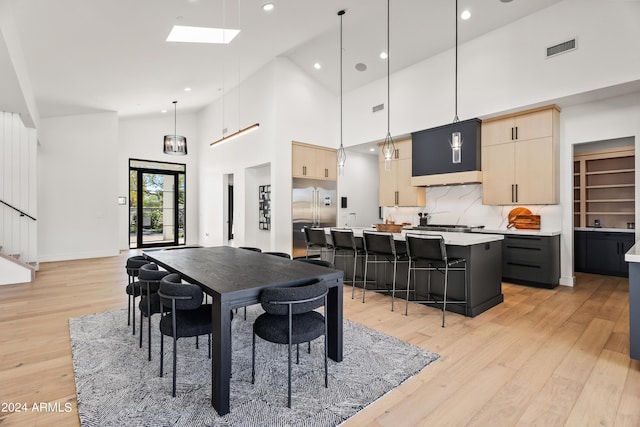 dining area featuring high vaulted ceiling, a skylight, and light hardwood / wood-style flooring