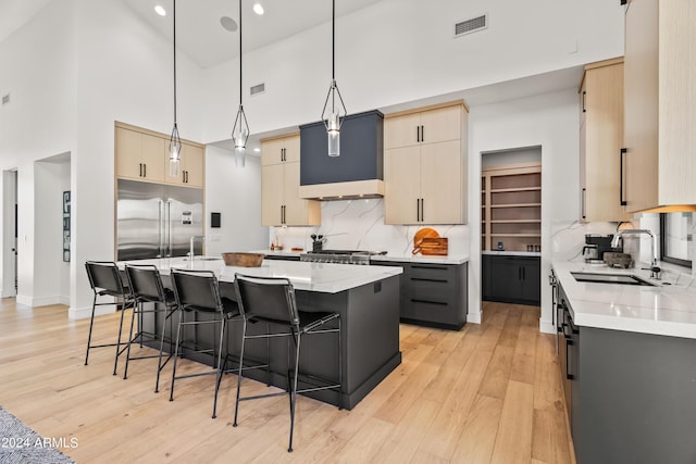 kitchen featuring a center island with sink, a breakfast bar, hanging light fixtures, stainless steel built in fridge, and high vaulted ceiling