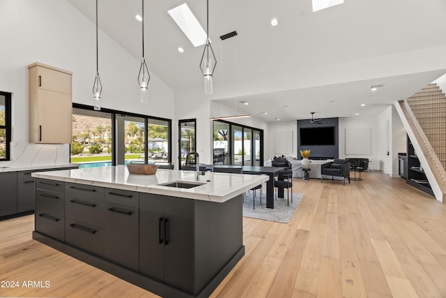 kitchen with a skylight, ceiling fan, sink, a kitchen island with sink, and high vaulted ceiling