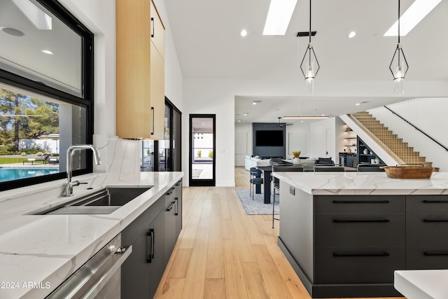 kitchen featuring ceiling fan, sink, hanging light fixtures, a skylight, and light stone counters