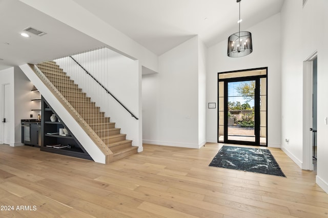 foyer entrance featuring a chandelier, a towering ceiling, and light hardwood / wood-style flooring