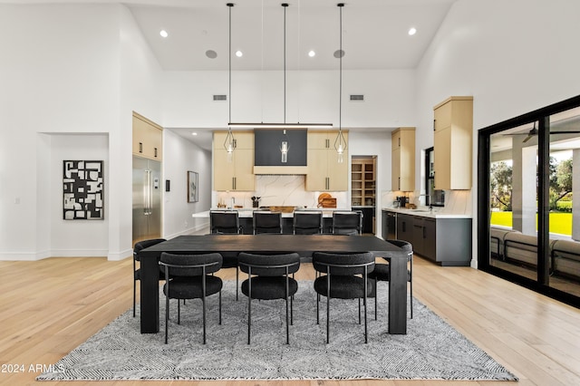 kitchen featuring a towering ceiling, light brown cabinets, tasteful backsplash, light hardwood / wood-style floors, and hanging light fixtures