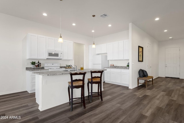 kitchen with white cabinets, light stone countertops, white appliances, dark hardwood / wood-style floors, and a kitchen island with sink