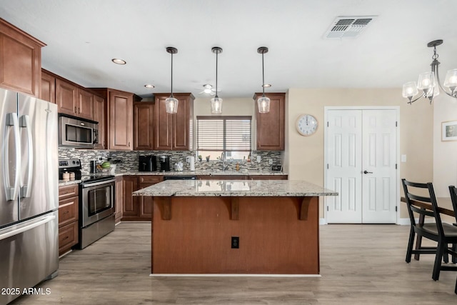 kitchen with stainless steel appliances, a center island, hanging light fixtures, and light stone countertops