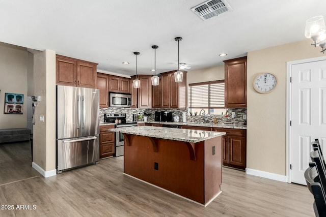 kitchen featuring sink, light stone counters, a center island, pendant lighting, and stainless steel appliances