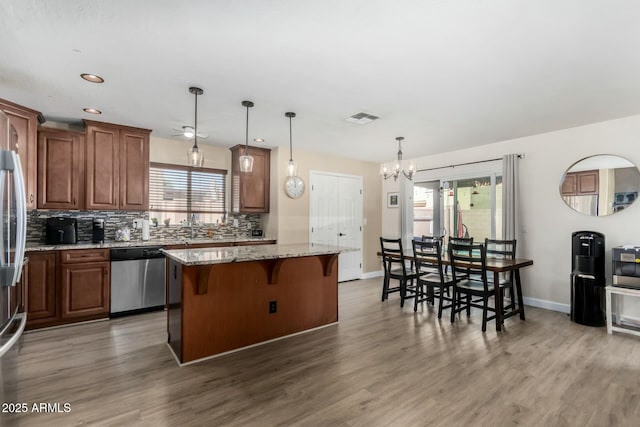 kitchen with pendant lighting, dishwasher, a center island, light stone countertops, and decorative backsplash