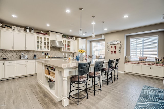 kitchen with a kitchen breakfast bar, white cabinetry, a center island with sink, and hanging light fixtures