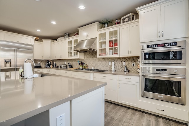 kitchen with appliances with stainless steel finishes, sink, light hardwood / wood-style flooring, white cabinets, and range hood