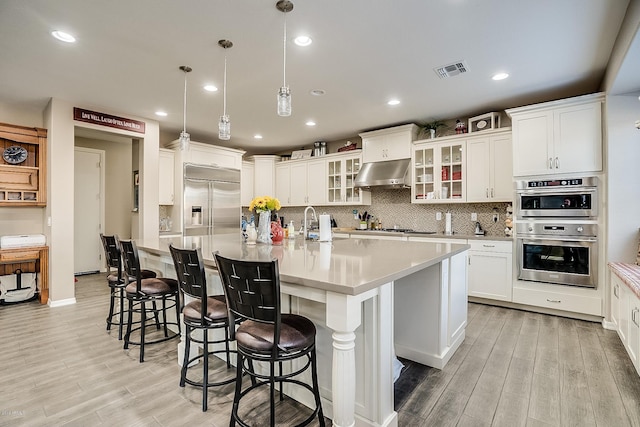 kitchen with appliances with stainless steel finishes, a spacious island, exhaust hood, white cabinetry, and hanging light fixtures