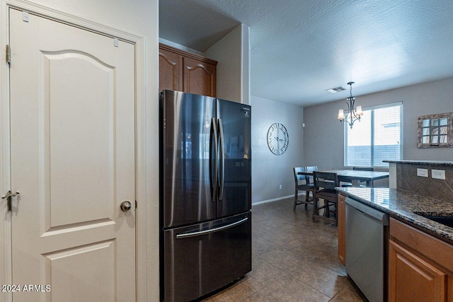 kitchen with an inviting chandelier, appliances with stainless steel finishes, light tile patterned flooring, pendant lighting, and a textured ceiling