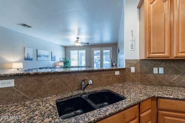 kitchen featuring dark stone counters, a textured ceiling, backsplash, sink, and ceiling fan