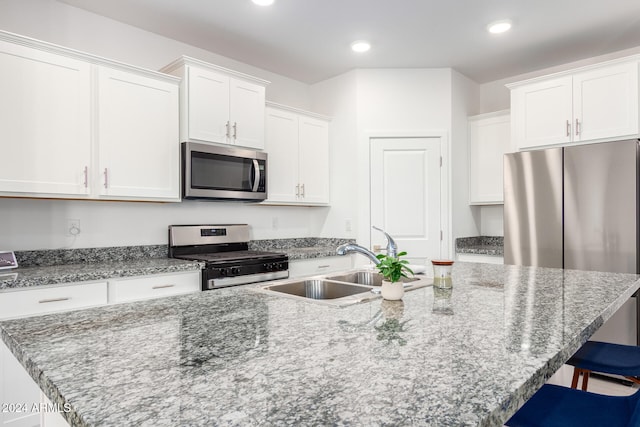 kitchen featuring white cabinets, a kitchen island with sink, a kitchen bar, sink, and stainless steel appliances