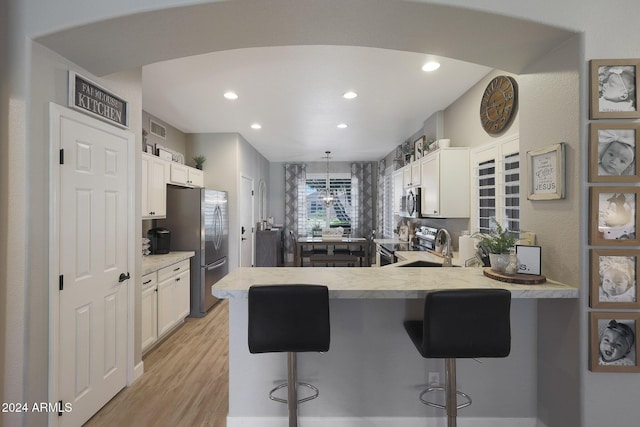 kitchen with light hardwood / wood-style floors, a kitchen bar, kitchen peninsula, and appliances with stainless steel finishes