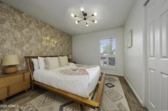 bedroom with baseboards, a chandelier, wallpapered walls, and wood finished floors