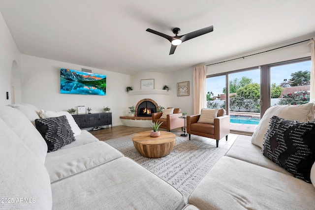 living area with ceiling fan, wood finished floors, arched walkways, and a tile fireplace