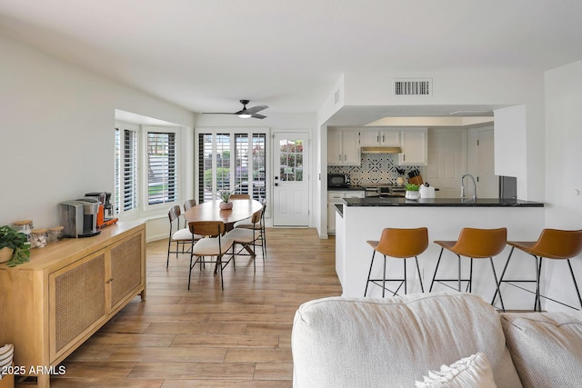 kitchen featuring a kitchen breakfast bar, visible vents, light wood-style flooring, black microwave, and a ceiling fan