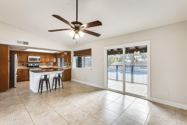 kitchen featuring vaulted ceiling, a kitchen island, a breakfast bar, decorative backsplash, and stainless steel appliances