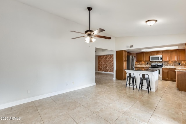 kitchen featuring a kitchen bar, decorative backsplash, a center island, ceiling fan, and stainless steel appliances