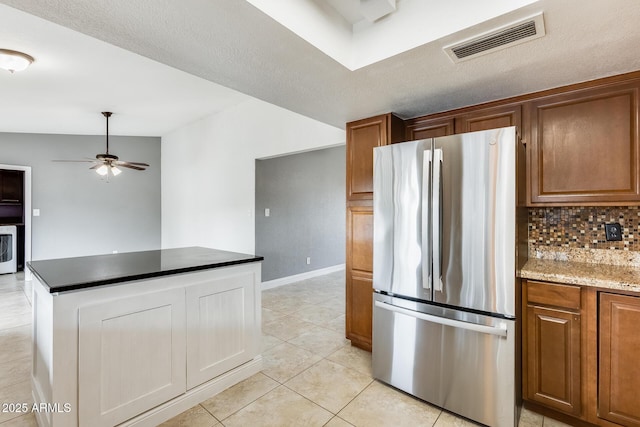 kitchen with tasteful backsplash, dark stone countertops, light tile patterned floors, stainless steel fridge, and ceiling fan