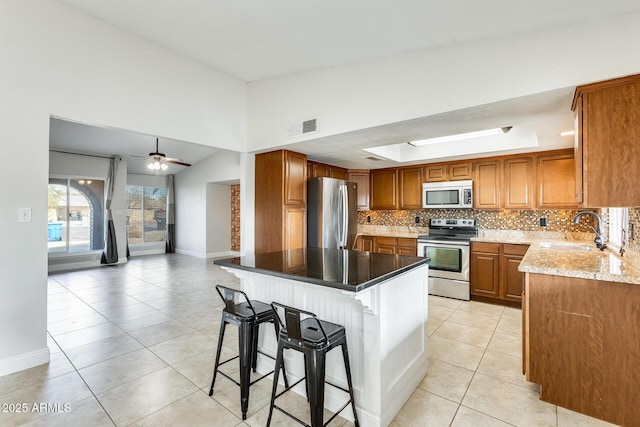 kitchen featuring sink, a breakfast bar area, decorative backsplash, light stone counters, and stainless steel appliances