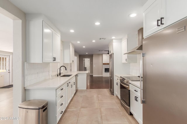 kitchen featuring sink, stainless steel appliances, wall chimney range hood, backsplash, and white cabinets