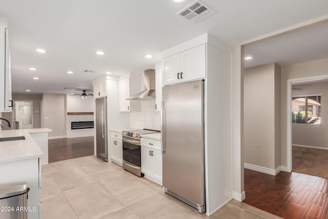 kitchen featuring stainless steel appliances, ceiling fan, sink, wall chimney range hood, and white cabinets