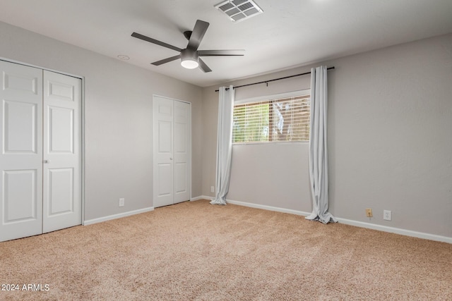 unfurnished bedroom with ceiling fan, light colored carpet, and multiple closets