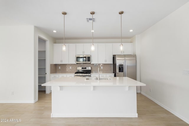 kitchen featuring stainless steel appliances, sink, decorative light fixtures, a center island with sink, and white cabinets