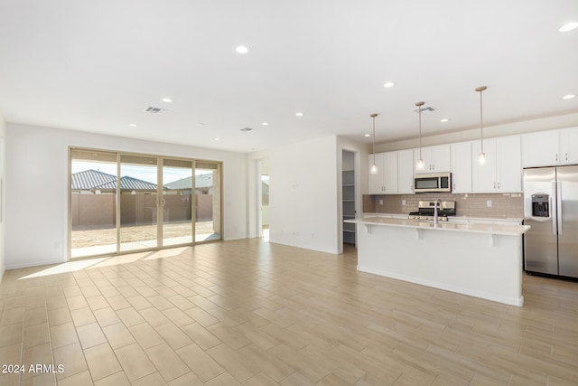 kitchen featuring appliances with stainless steel finishes, tasteful backsplash, a kitchen island with sink, decorative light fixtures, and white cabinetry