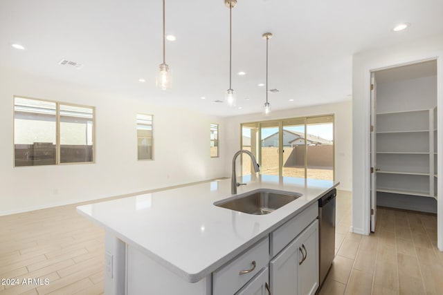 kitchen featuring stainless steel dishwasher, a kitchen island with sink, sink, decorative light fixtures, and light hardwood / wood-style floors