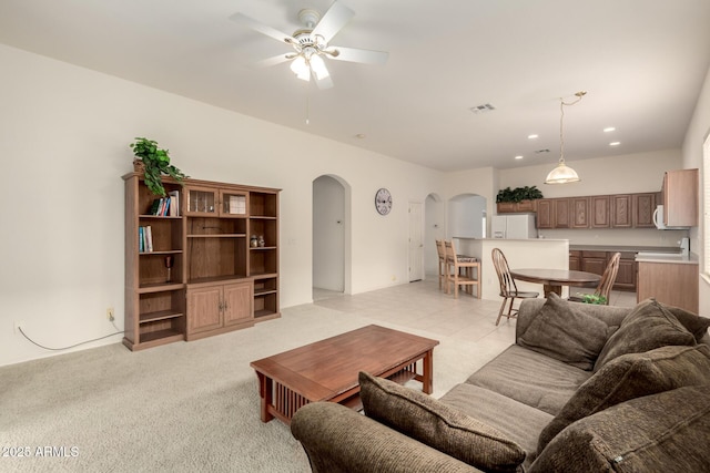 living area with visible vents, arched walkways, light colored carpet, and ceiling fan