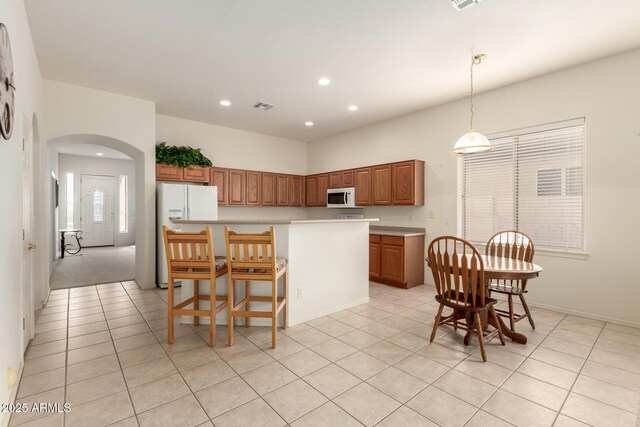 kitchen featuring visible vents, a center island, brown cabinetry, arched walkways, and white appliances