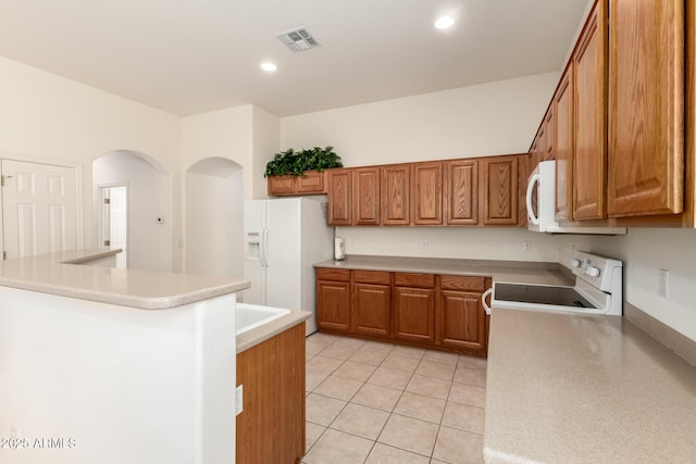 kitchen featuring light tile patterned flooring, visible vents, brown cabinets, and white appliances