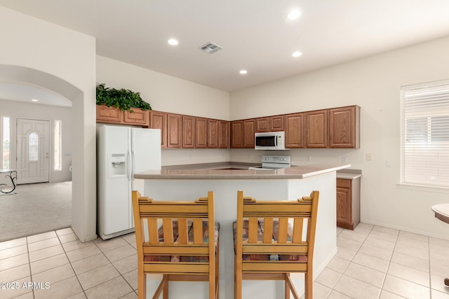 kitchen featuring visible vents, a kitchen island, light tile patterned flooring, arched walkways, and white appliances