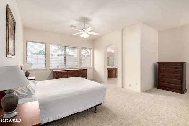 bedroom with visible vents, arched walkways, light colored carpet, and ensuite bath