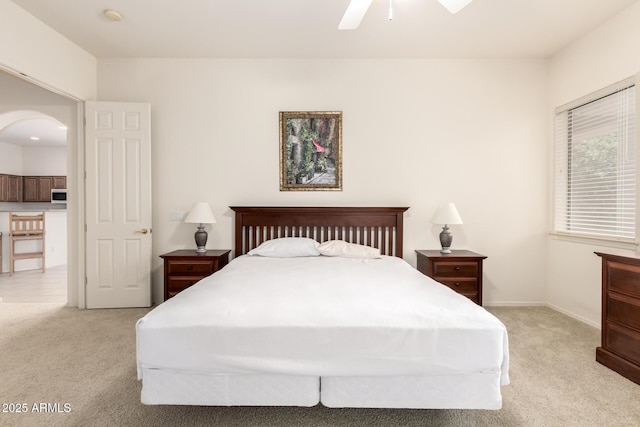 bedroom with baseboards, light carpet, arched walkways, and ceiling fan