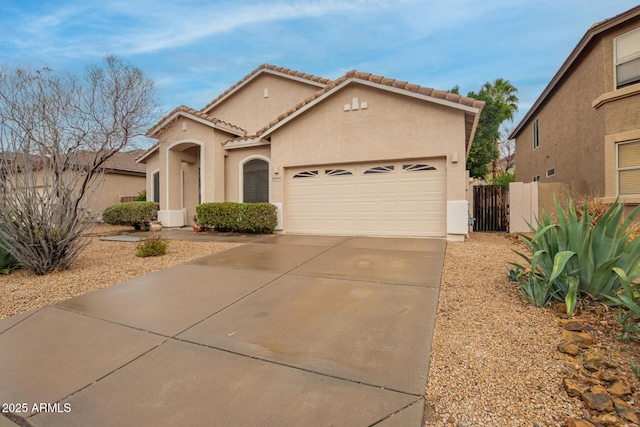 mediterranean / spanish-style home with an attached garage, fence, a tiled roof, stucco siding, and driveway