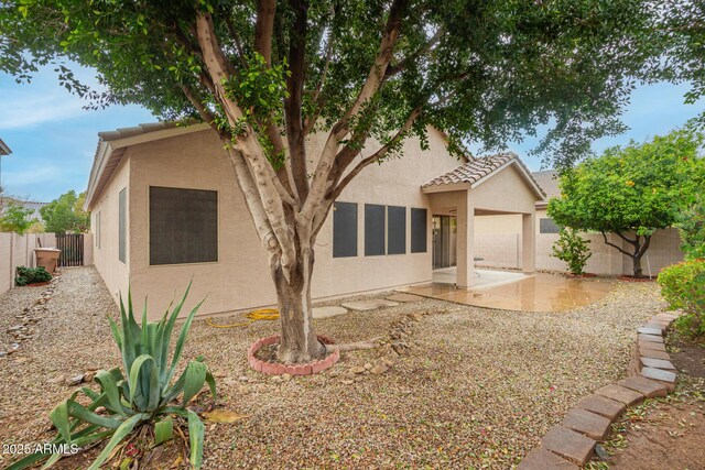 view of front facade with a tiled roof, a patio area, a fenced backyard, and stucco siding