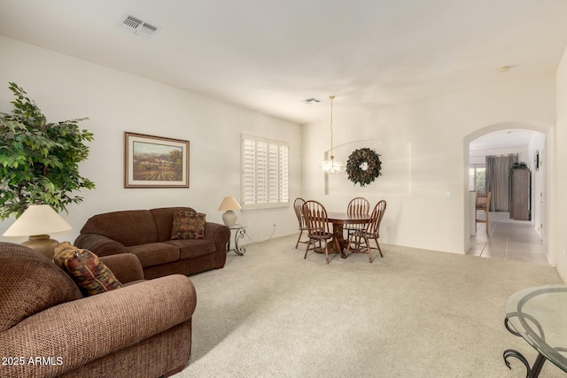 carpeted living room featuring arched walkways, visible vents, tile patterned floors, and an inviting chandelier