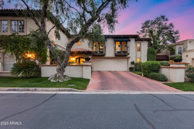 mediterranean / spanish-style home featuring a balcony, stucco siding, a garage, driveway, and a tiled roof