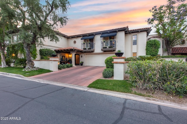 mediterranean / spanish house featuring a balcony, stucco siding, concrete driveway, a garage, and a tiled roof
