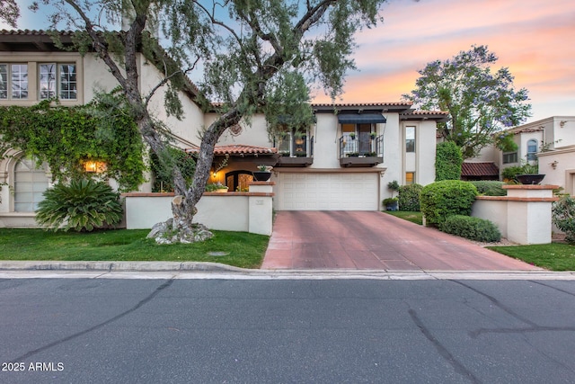 mediterranean / spanish house featuring a balcony, stucco siding, a tile roof, driveway, and an attached garage