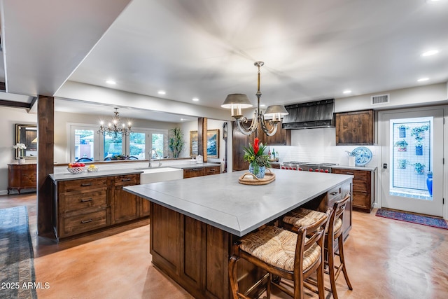 kitchen featuring a chandelier, wall chimney range hood, a spacious island, a sink, and light countertops