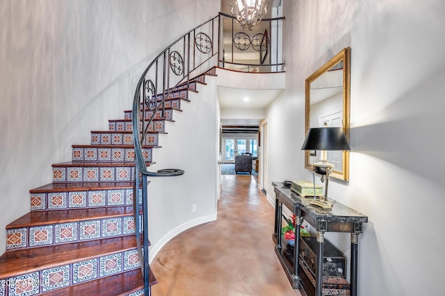 staircase with concrete flooring, a high ceiling, a chandelier, and baseboards
